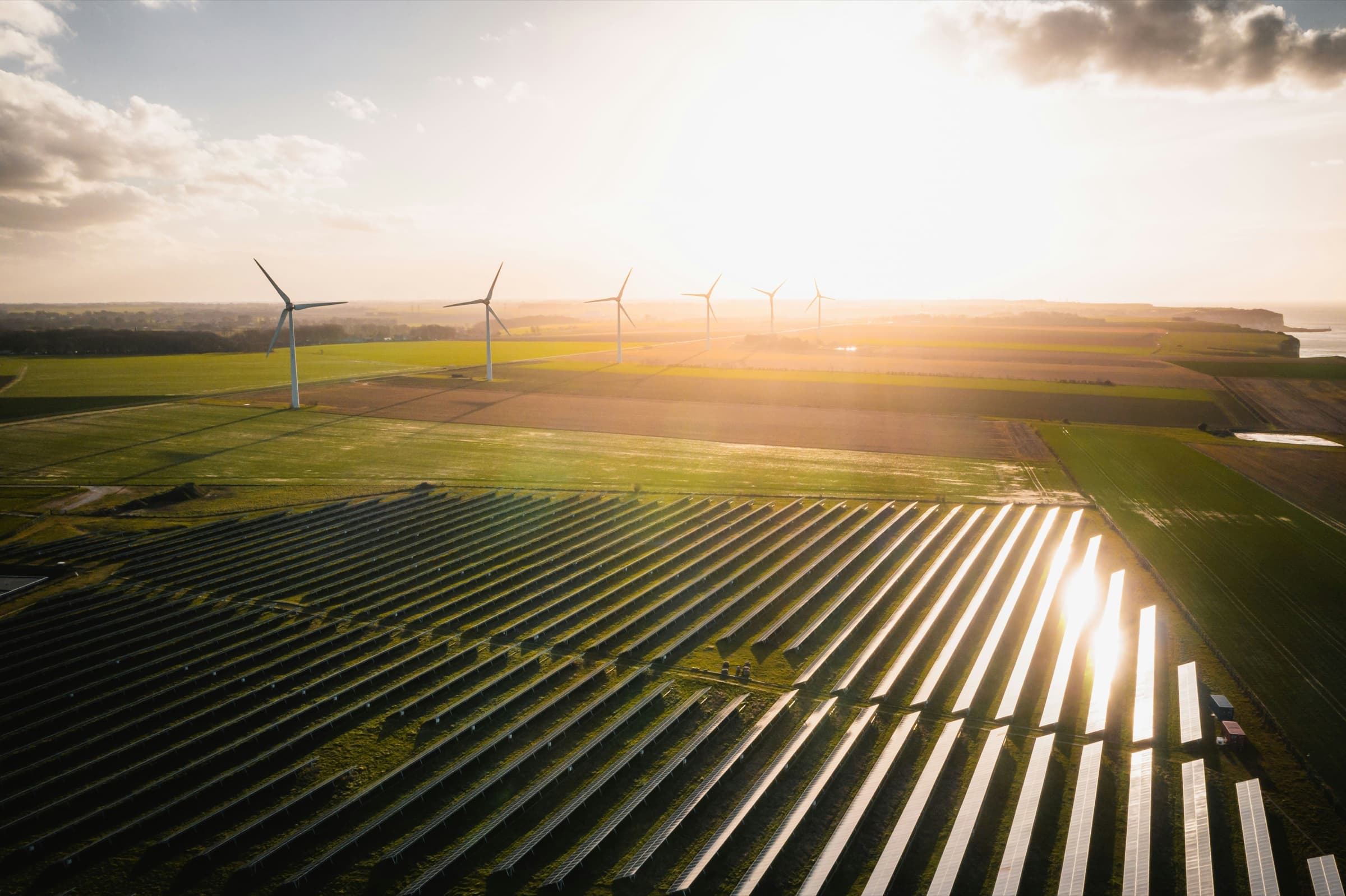 Wind turbines and a solar field at sunset over rolling farmland